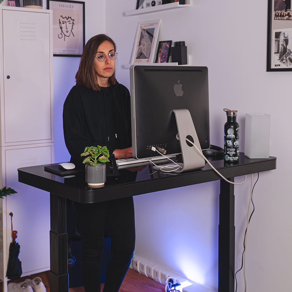 Bureau assis-debout CONNECT avec plateau en verre trempé noir, vue de trois-quarts montrant la structure métallique.