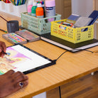 Dessin numérique et matériel créatif disposés sur un bureau assis debout, plateau bois avec tablette graphique et accessoires d’art