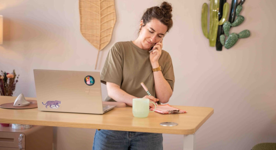 Bureau assis debout LIFT KQUEO blanc et chêne clair en position debout avec utilisateur travaillant et prenant des notes